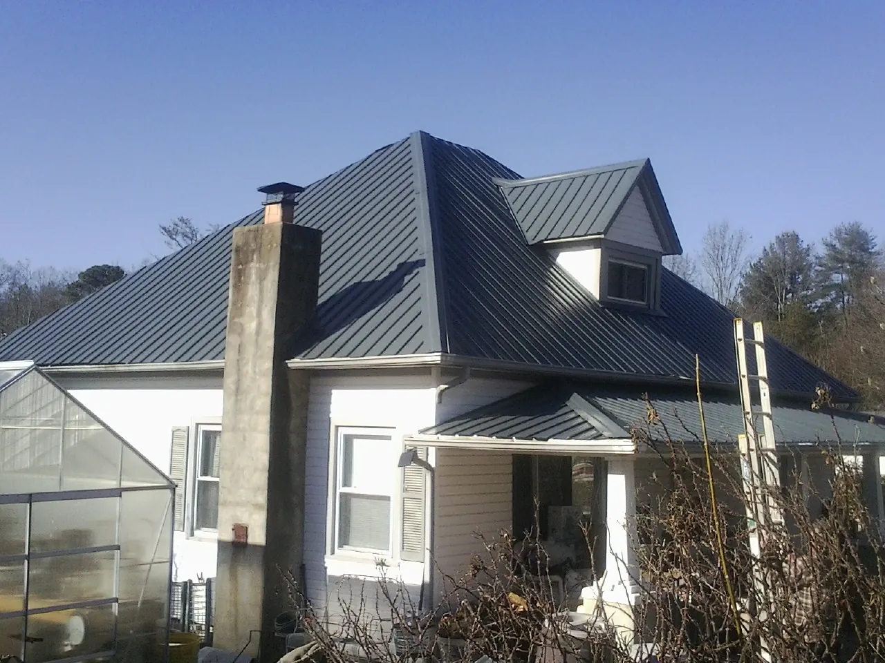 Dark blue standing seam metal roof on a white farmhouse with dormer — Slate & Tile Roof Repair by Roofing Brothers in Krum