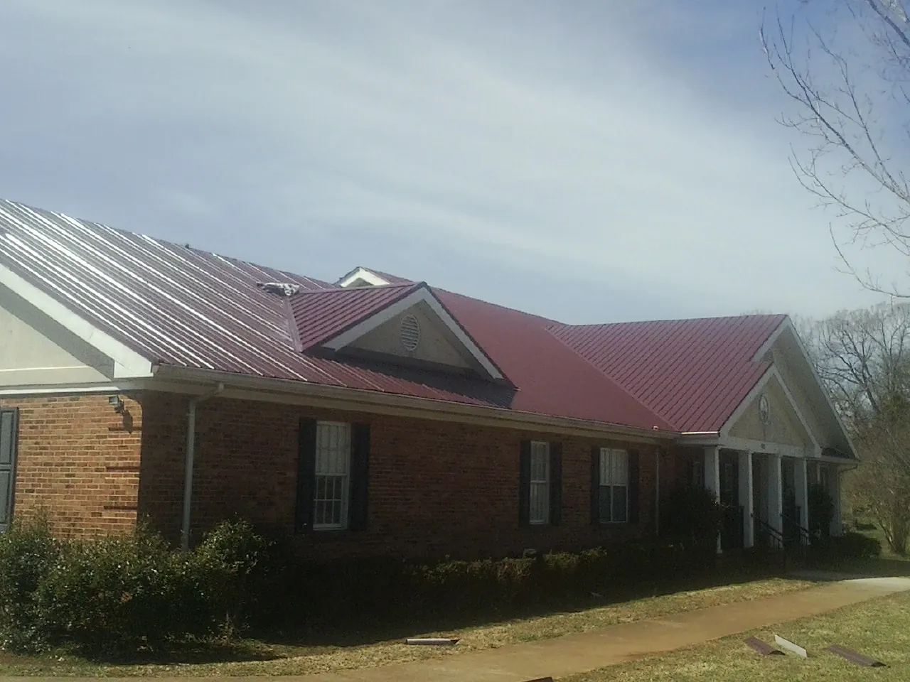 Red metal roof with gabled entries on a long brick building, from a Hail Damage Roof Repair job in Krum