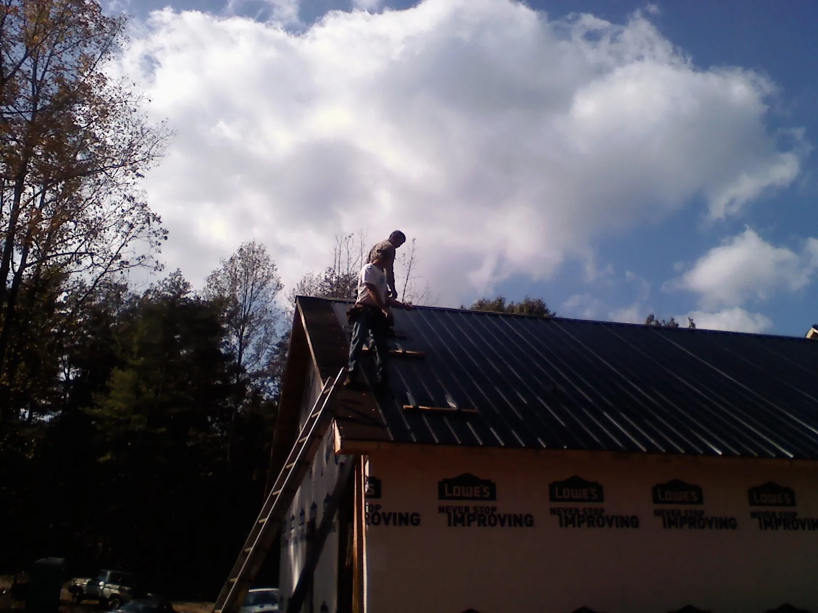 Roofer fastening dark metal panels high against a cloudy sky, from a Roof Inspection job in Krum